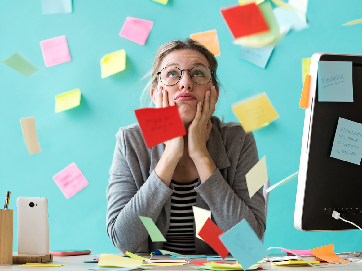 An exasperated office worker at a desk buried under a flurry of sticky notes
